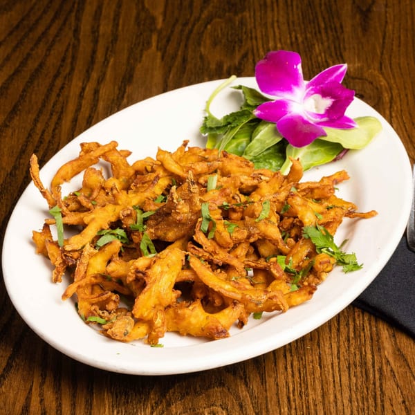 Crispy onion bhaji, an Indian appetizer, garnished with cilantro and a purple orchid on a white plate.