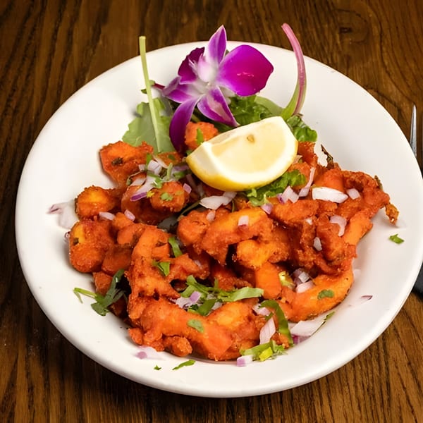 Indian chicken pakora with red onions, cilantro, a lemon wedge, and an orchid garnish.