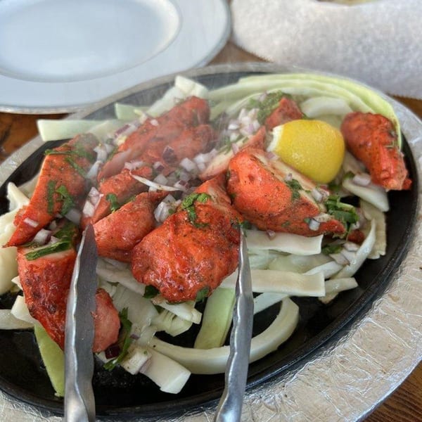 Sizzling red tandoori chicken pieces with onions, cilantro, and a lemon wedge on a hot plate.