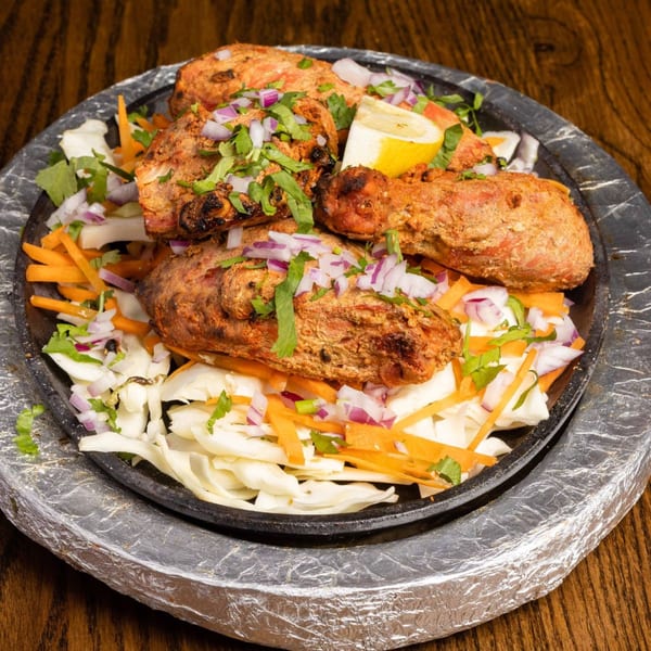Indian chicken tikka, garnished with red onions, cilantro, and a lemon wedge, on a sizzling platter.