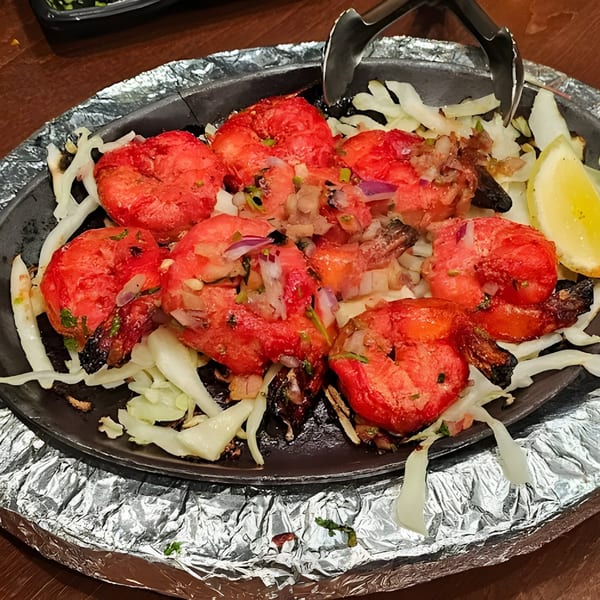 Sizzling tandoori shrimp with onions, cabbage, and a lemon wedge on a hot plate.