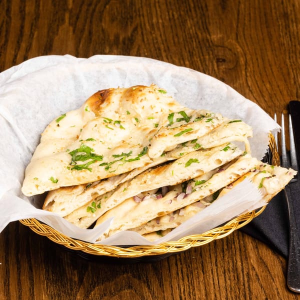 Basket of freshly baked garlic naan bread with herbs and onions on a wooden table.