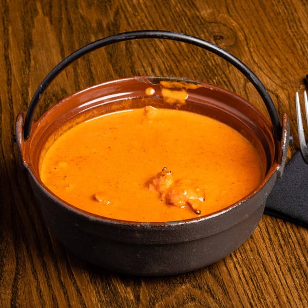 A black cast iron pot filled with orange Indian curry, on a wooden table.